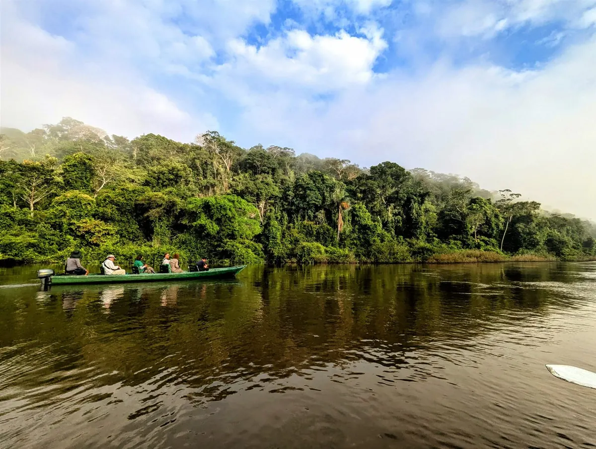 A small boat crossing a black-water river at sunrise, mist rising over the forest wall